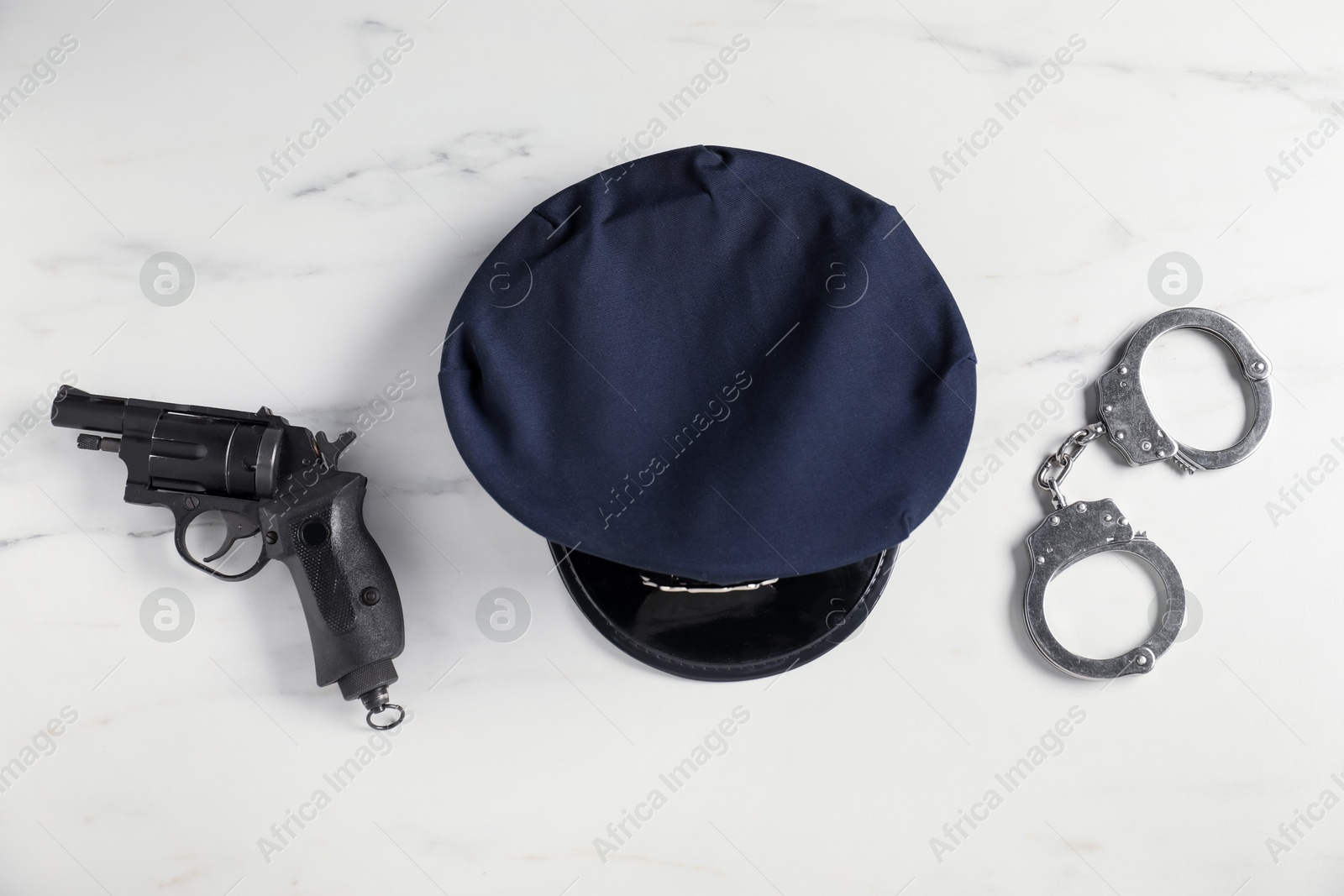 Police cap, gun and handcuffs on white marble table, flat lay Photo of Police cap, gun and handcuffs on white marble table, flat lay