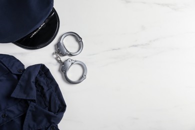Photo of Police uniform and handcuffs on white marble table, flat lay. Space for text