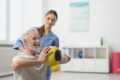 Photo of Doctor and patient exercising with medicine ball in clinic, space for text