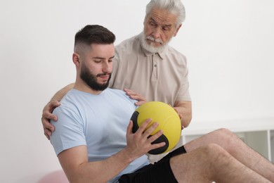 Photo of Doctor and patient exercising with medicine ball in clinic