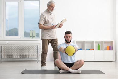 Photo of Doctor and patient exercising with medicine ball in clinic