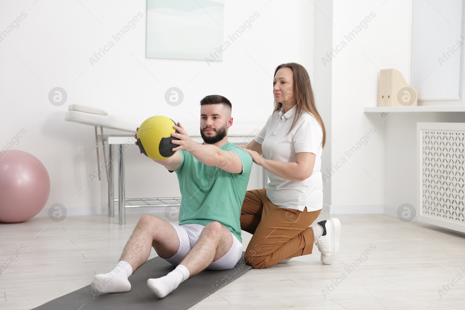 Photo of Doctor and patient exercising with medicine ball in clinic