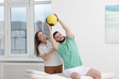 Photo of Doctor and patient exercising with medicine ball in clinic