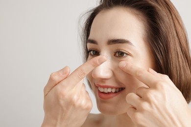 Photo of Woman putting in contact lens on light background, closeup