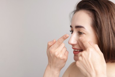 Photo of Woman putting in contact lens on light background. Space for text