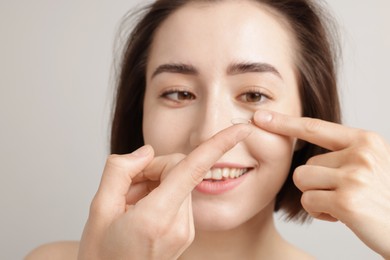 Photo of Woman putting in contact lens on light background, closeup