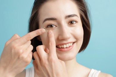 Photo of Woman putting in contact lens on light blue background, closeup