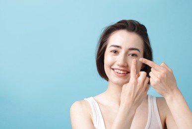 Photo of Woman putting in contact lens on light blue background. Space for text