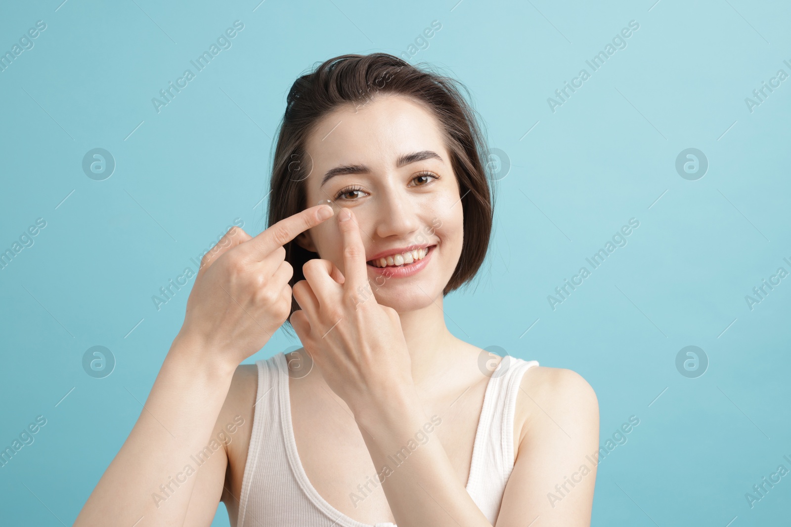 Woman putting in contact lens on light blue background Photo of Woman putting in contact lens on light blue background