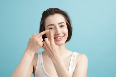 Photo of Woman putting in contact lens on light blue background