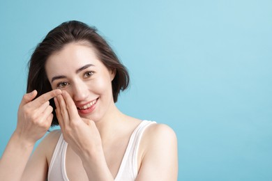 Photo of Woman putting in contact lens on light blue background. Space for text