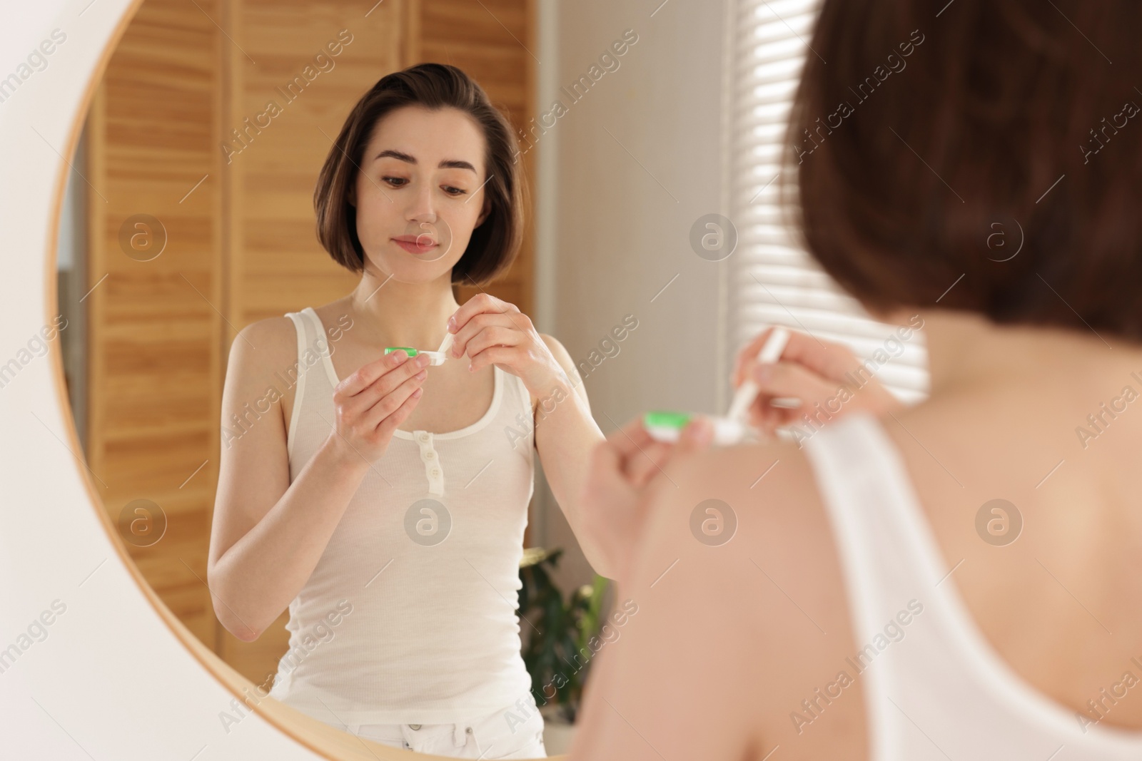 Woman taking contact lens out of case near mirror indoors Photo of Woman taking contact lens out of case near mirror indoors