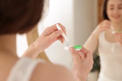 Photo of Woman taking contact lens out of case indoors, closeup