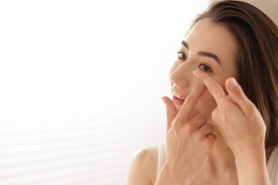 Photo of Beautiful woman putting in contact lens indoors. Space for text