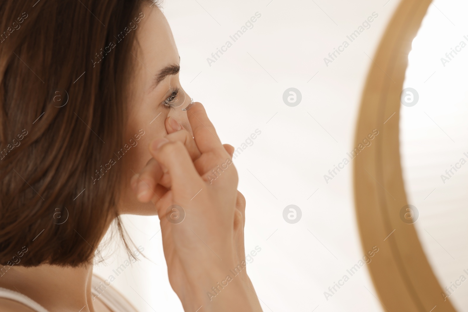 Woman putting in contact lens near mirror indoors Photo of Woman putting in contact lens near mirror indoors
