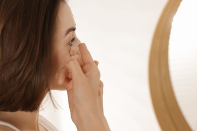 Photo of Woman putting in contact lens near mirror indoors
