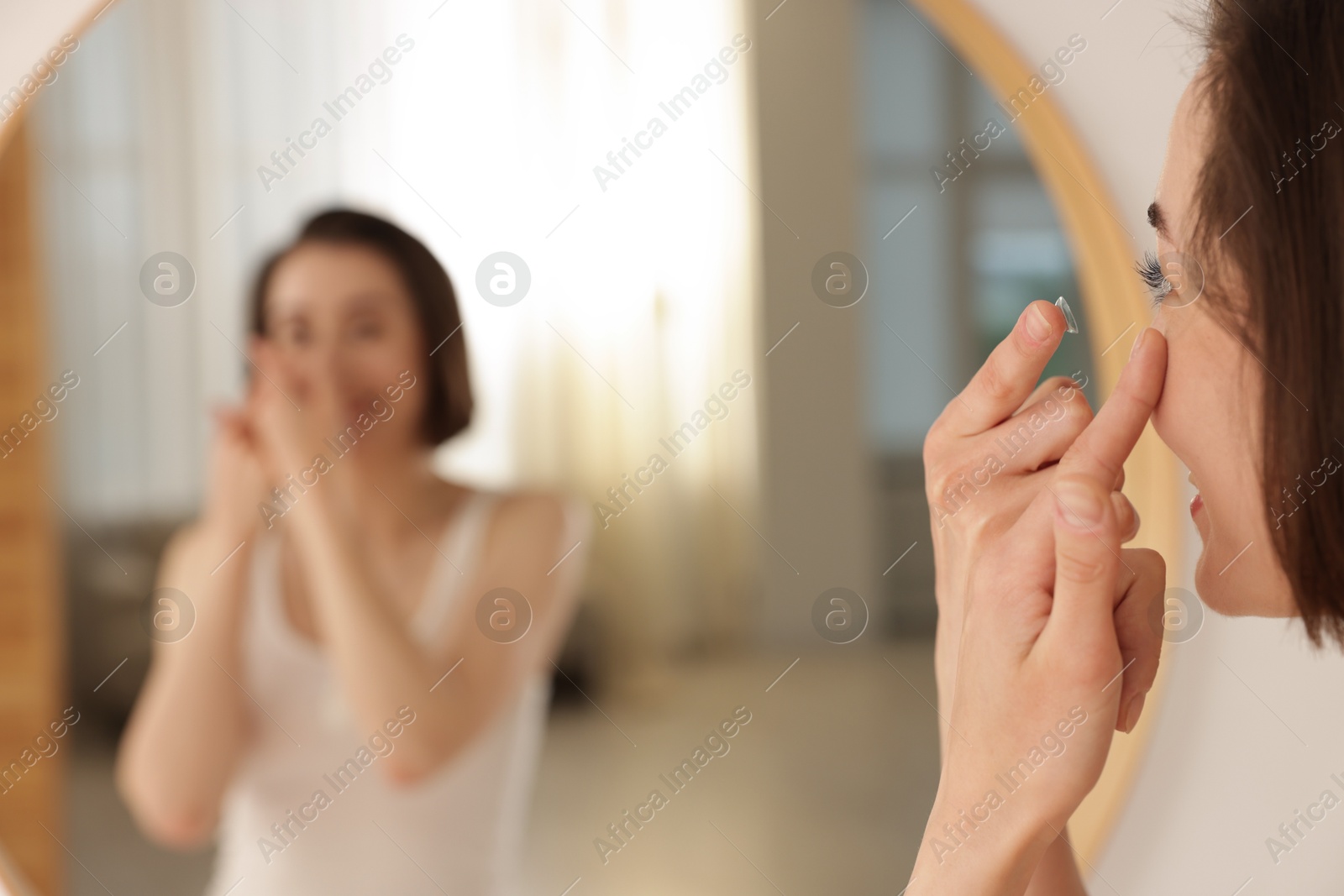 Woman putting in contact lens near mirror indoors, selective focus Photo of Woman putting in contact lens near mirror indoors, selective focus