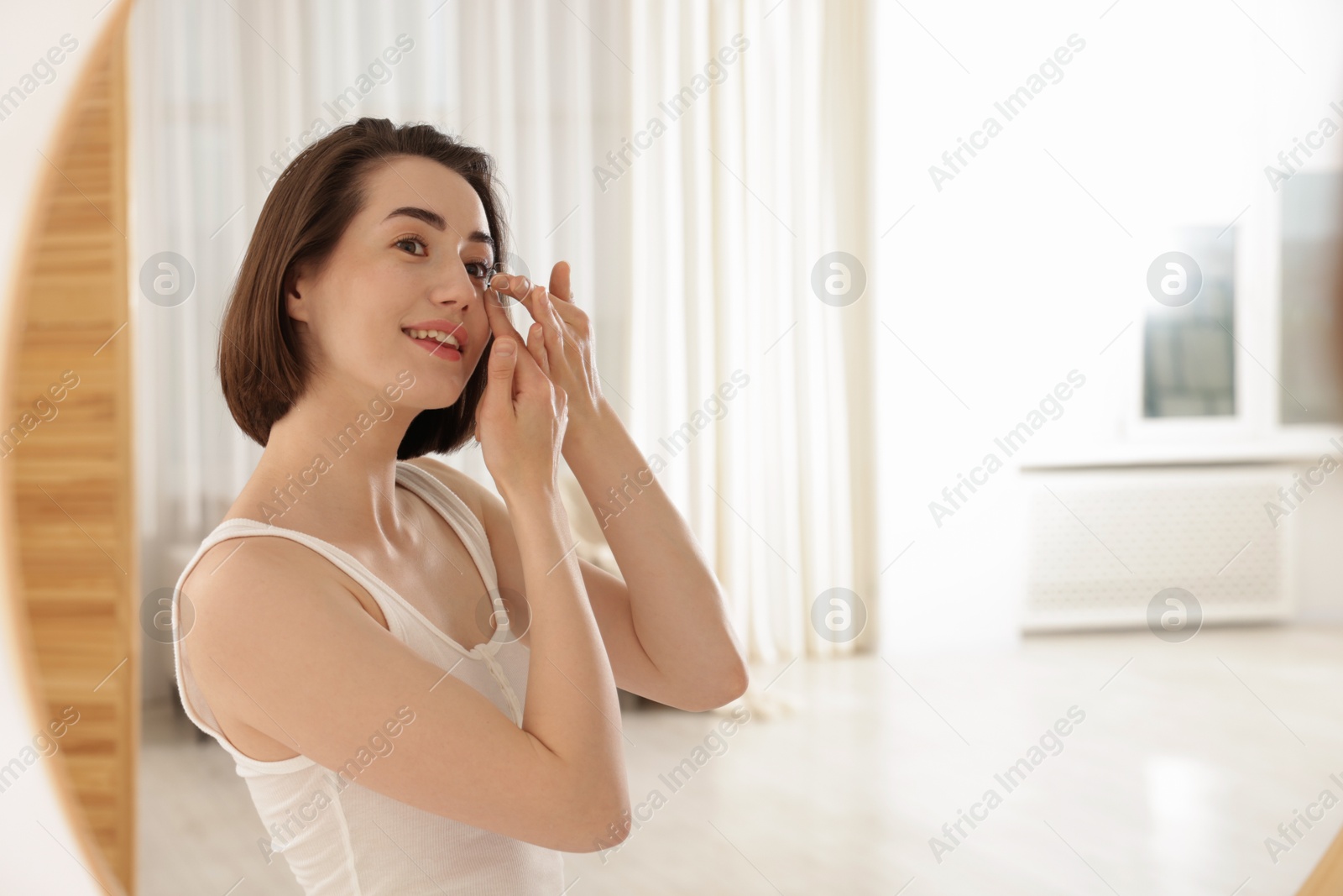 Woman putting in contact lens near mirror indoors Photo of Woman putting in contact lens near mirror indoors
