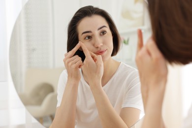 Photo of Woman putting in contact lens near mirror indoors