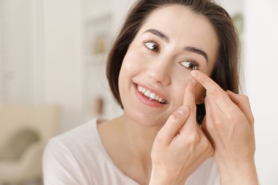 Photo of Beautiful woman putting in contact lens indoors