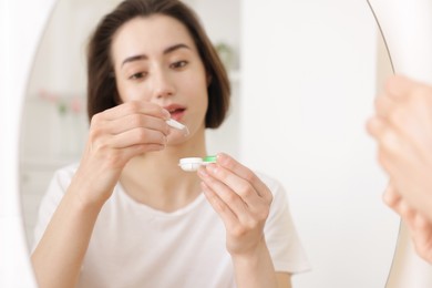 Photo of Woman taking contact lens out of case indoors, selective focus