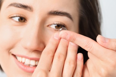 Photo of Woman putting in contact lens on light background, closeup