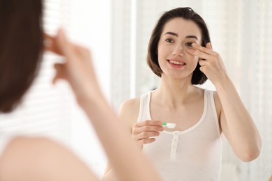 Photo of Woman putting in contact lens near mirror indoors