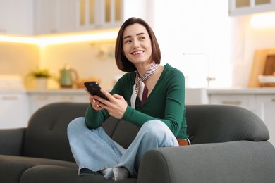 Photo of Woman using modern smartphone on sofa at home