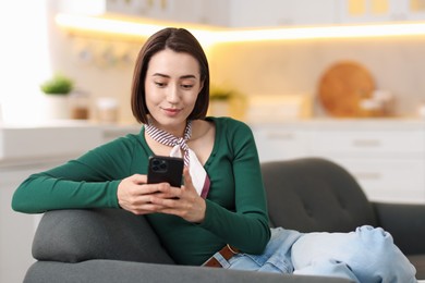 Photo of Woman using modern smartphone on sofa at home. Space for text
