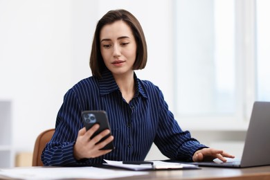 Photo of Beautiful woman using her smartphone while working at desk in office