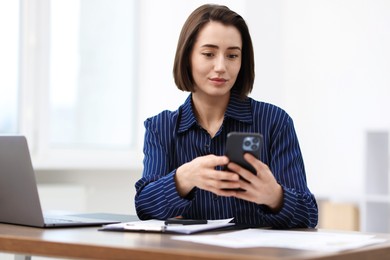 Photo of Beautiful woman using her smartphone while working at desk in office