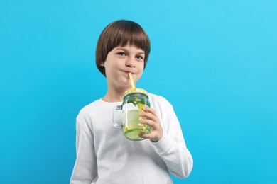 Photo of Cute little boy drinking lemonade on light blue background. Refreshing drink
