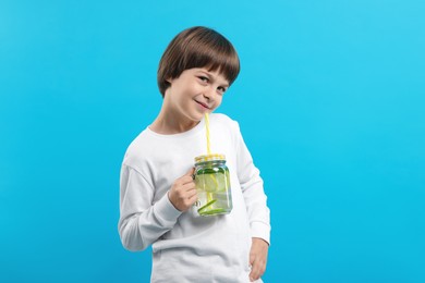 Photo of Cute little boy with mason jar of lemonade on light blue background. Refreshing drink