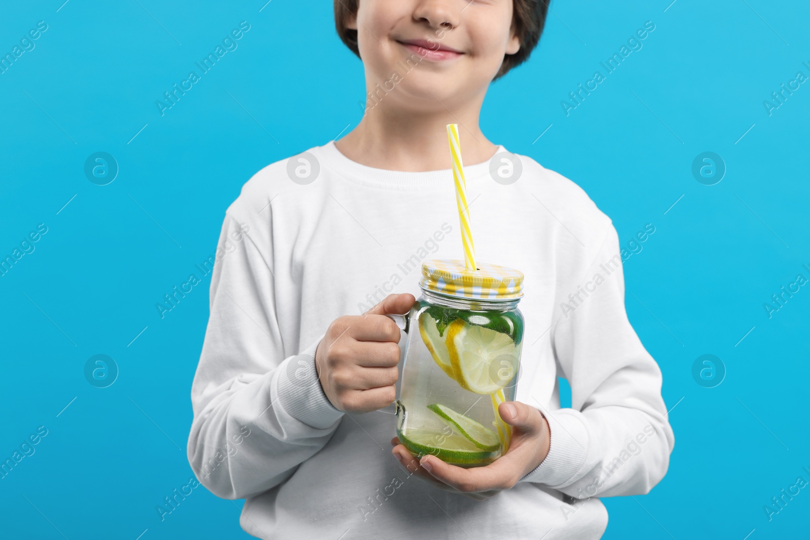 Little boy with mason jar of lemonade on light blue background, closeup. Refreshing drink Photo of Little boy with mason jar of lemonade on light blue background, closeup. Refreshing drink