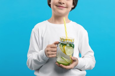 Photo of Little boy with mason jar of lemonade on light blue background, closeup. Refreshing drink