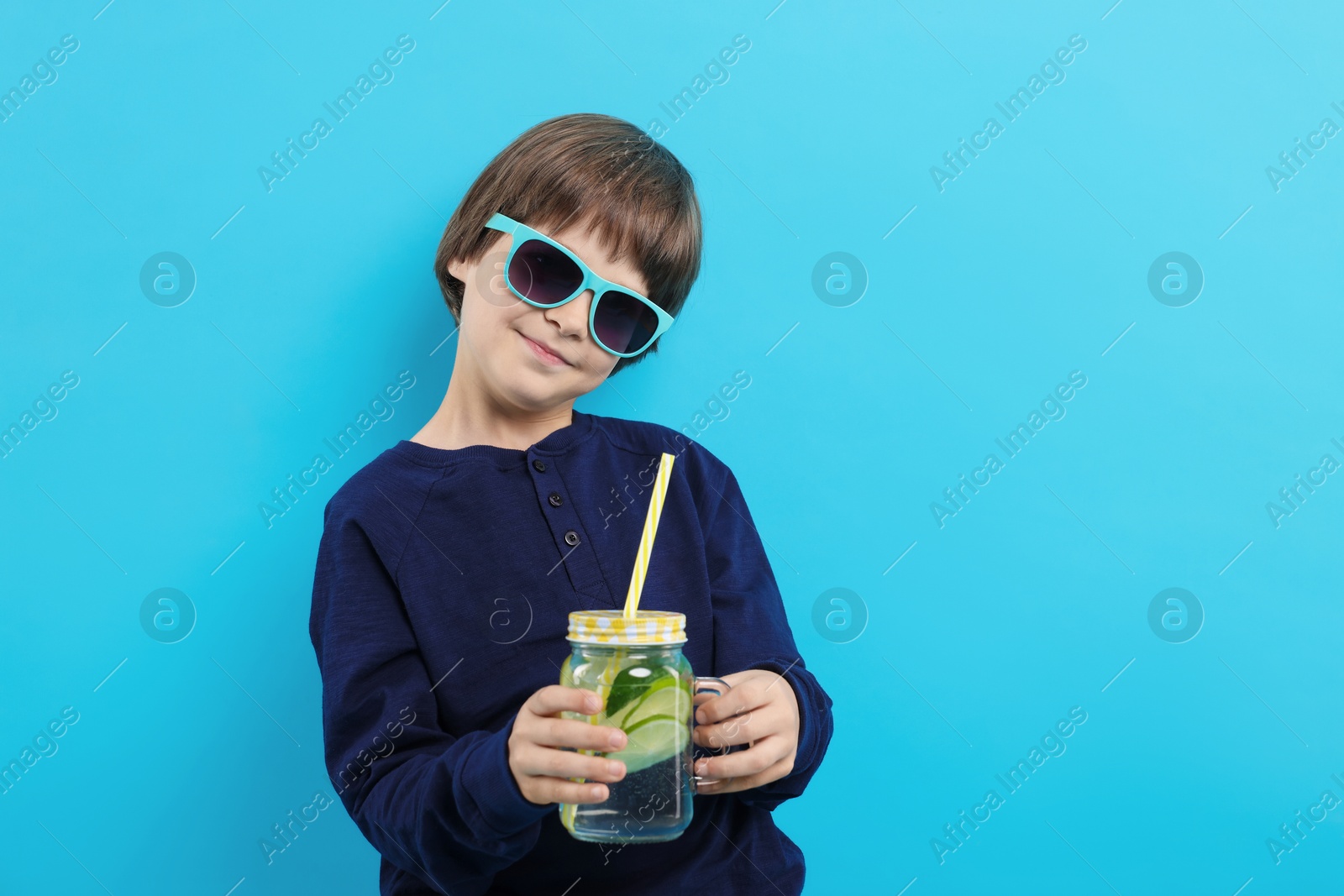 Cute little boy in sunglasses with mason jar of lemonade on light blue background. Refreshing drink Photo of Cute little boy in sunglasses with mason jar of lemonade on light blue background. Refreshing drink