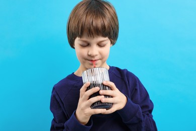 Photo of Cute little boy drinking refreshing soda on light blue background