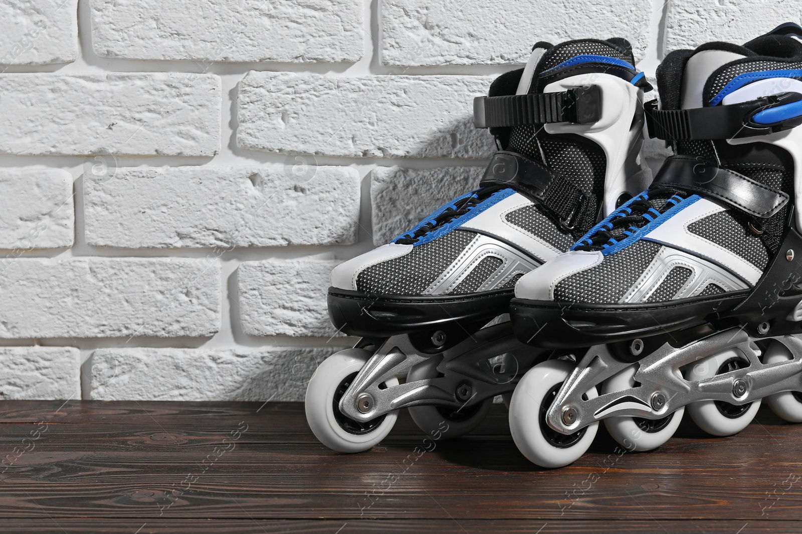 Photo of Pair of roller skates on wooden table near white brick wall, closeup. Space for text