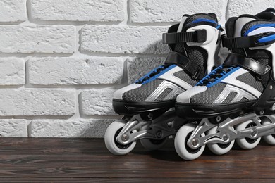Photo of Pair of roller skates on wooden table near white brick wall, closeup. Space for text