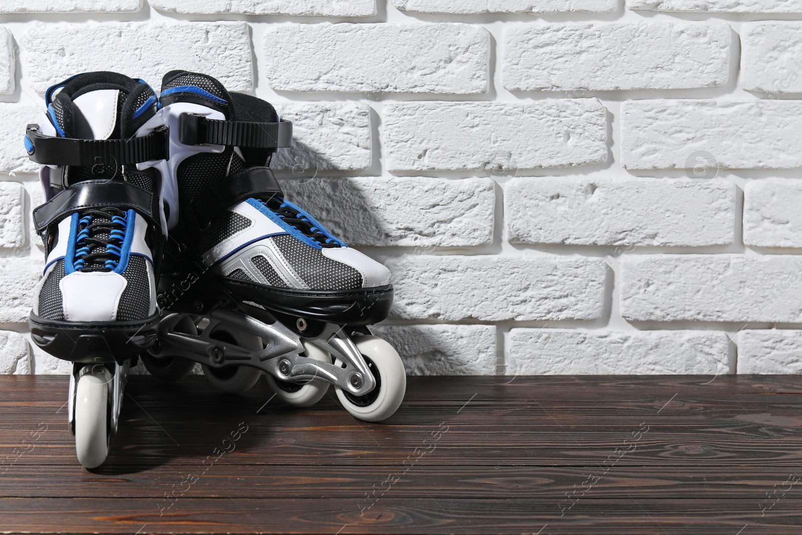 Pair of roller skates on wooden table near white brick wall, space for text Photo of Pair of roller skates on wooden table near white brick wall, space for text