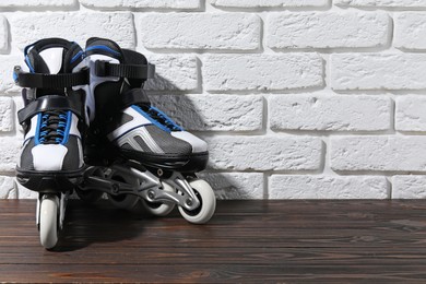 Photo of Pair of roller skates on wooden table near white brick wall, space for text