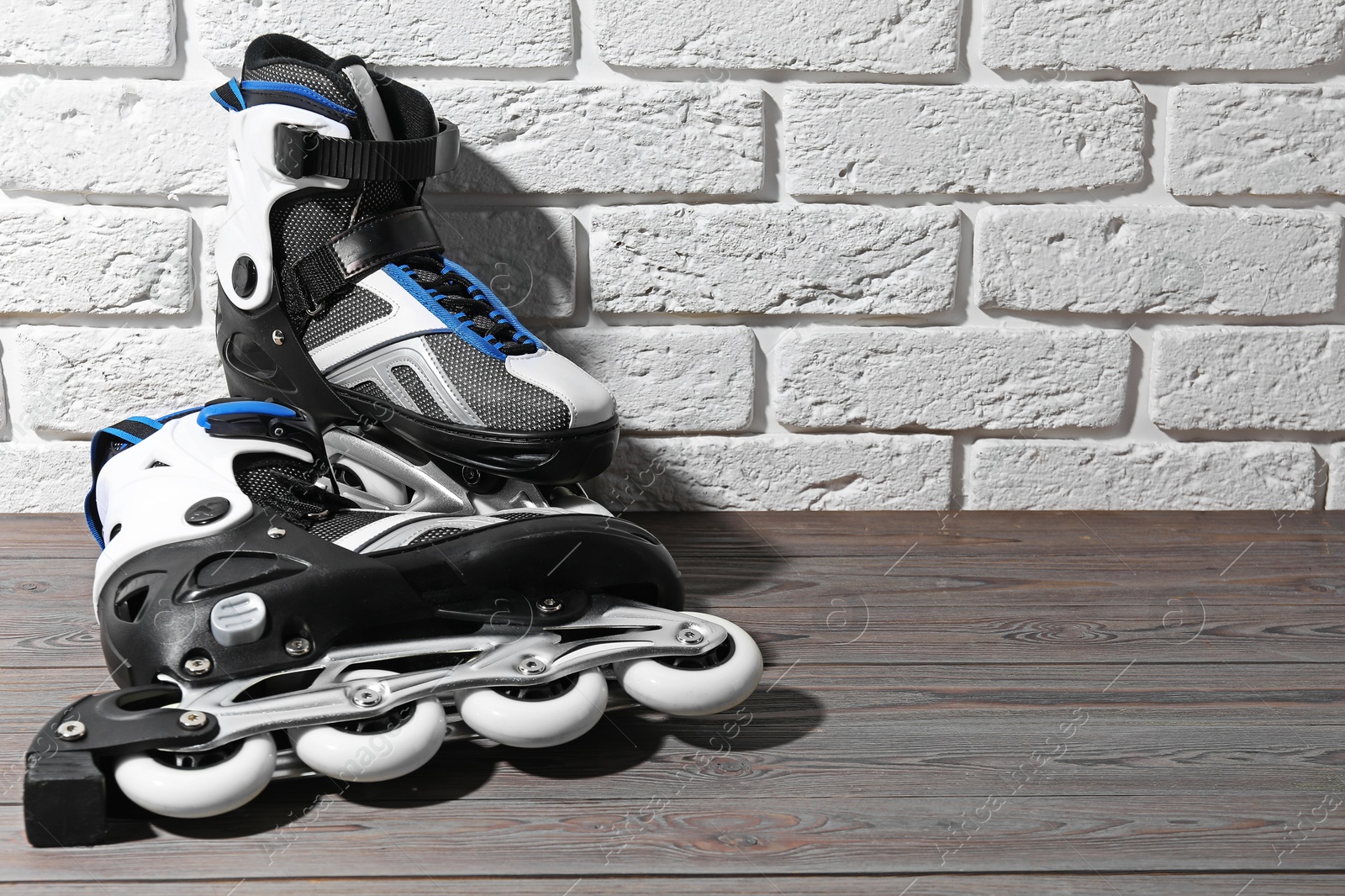 Pair of roller skates on wooden table near white brick wall, space for text Photo of Pair of roller skates on wooden table near white brick wall, space for text