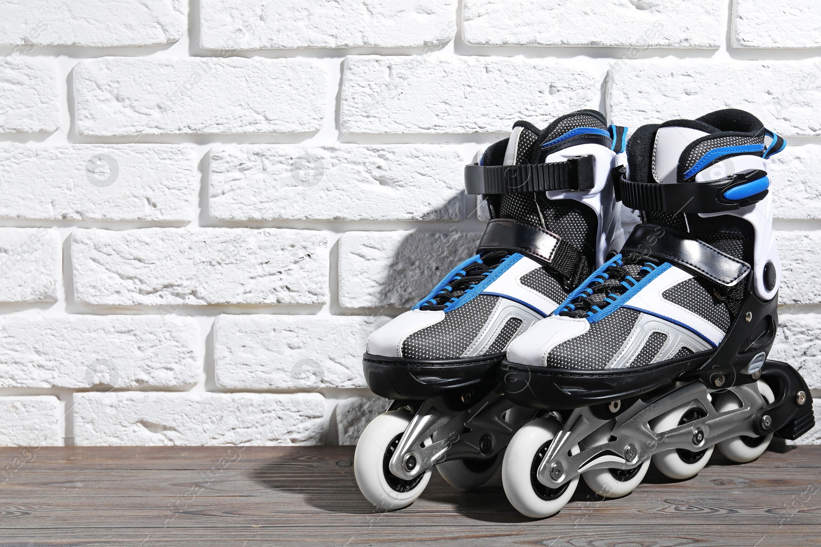 Pair of roller skates on wooden table near white brick wall, space for text Photo of Pair of roller skates on wooden table near white brick wall, space for text
