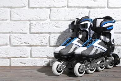 Photo of Pair of roller skates on wooden table near white brick wall, space for text