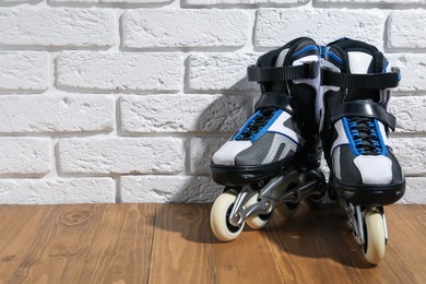 Photo of Pair of roller skates on wooden table near white brick wall, space for text