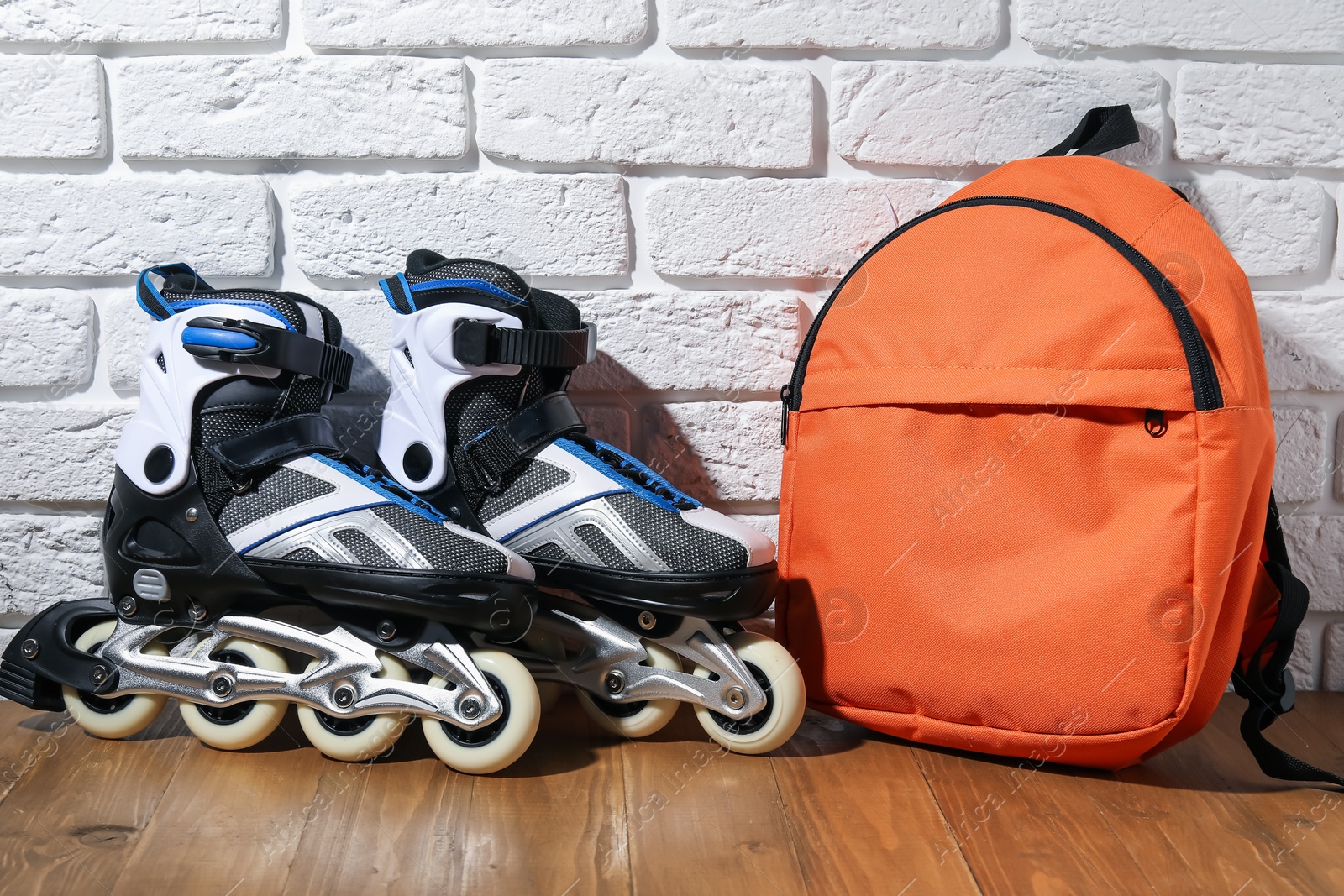 Pair of roller skates and backpack on wooden table near white brick wall Photo of Pair of roller skates and backpack on wooden table near white brick wall