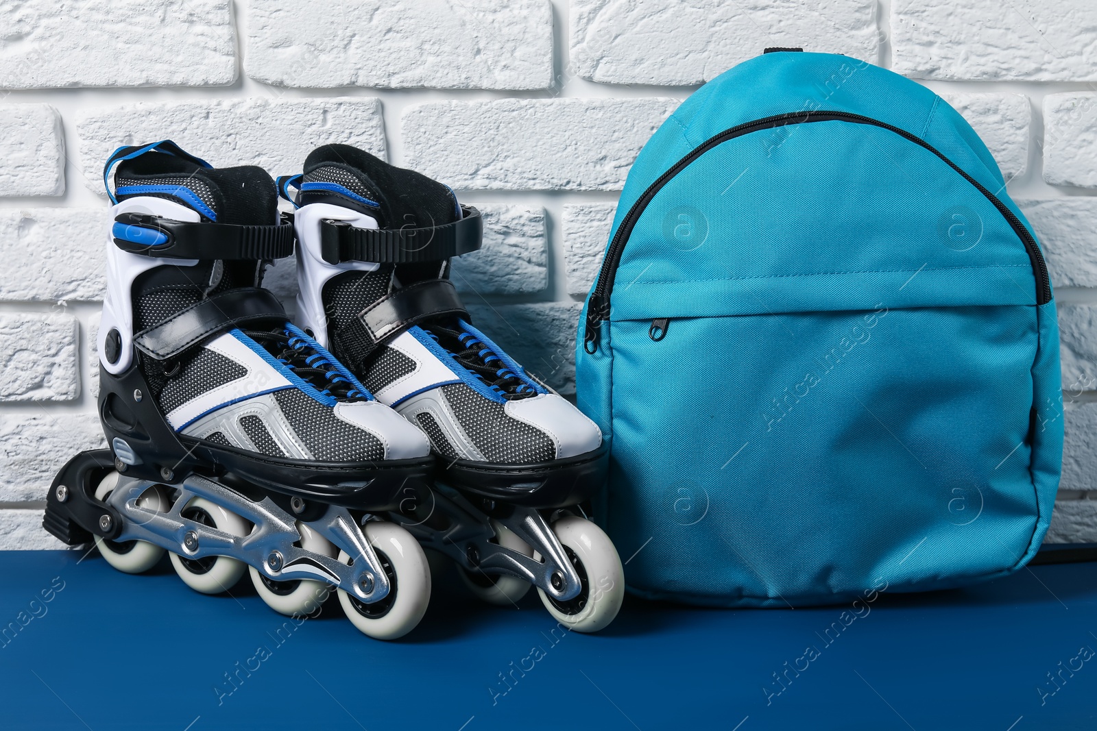 Pair of roller skates and backpack on blue table near white brick wall Photo of Pair of roller skates and backpack on blue table near white brick wall