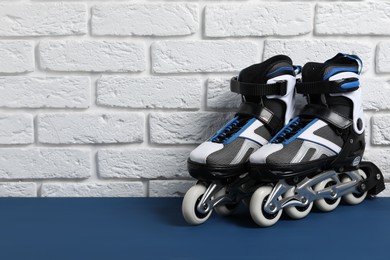 Photo of Pair of roller skates on blue table near white brick wall, space for text