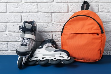 Photo of Pair of roller skates and backpack on blue table near white brick wall