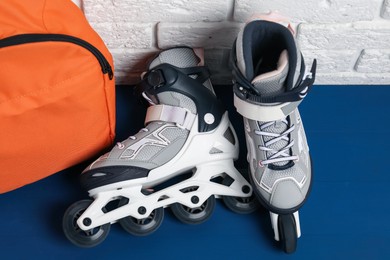 Photo of Pair of roller skates and backpack on blue table near white brick wall, above view